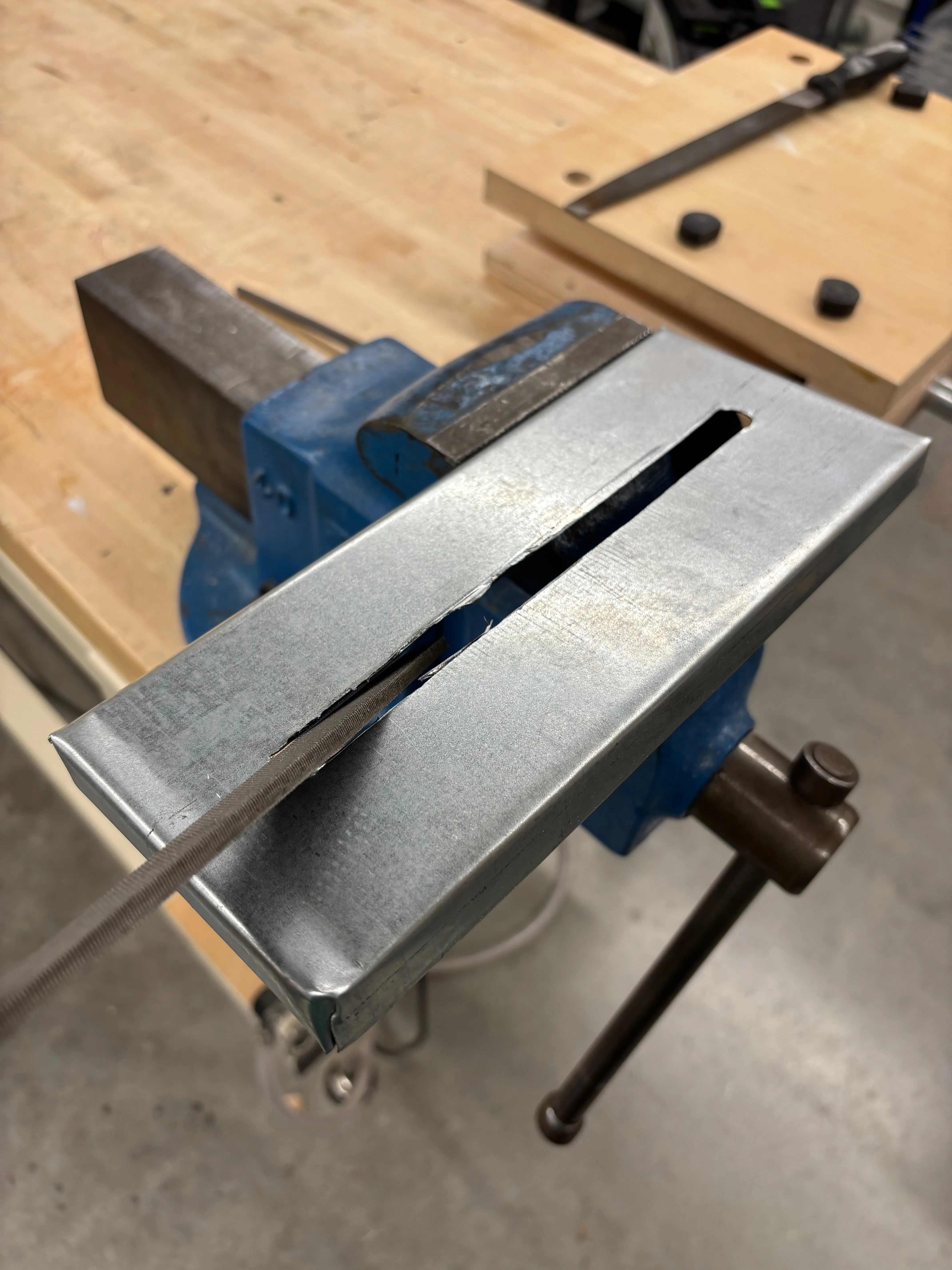 Top of sheet metal tissue box being filed as it is held in a vice