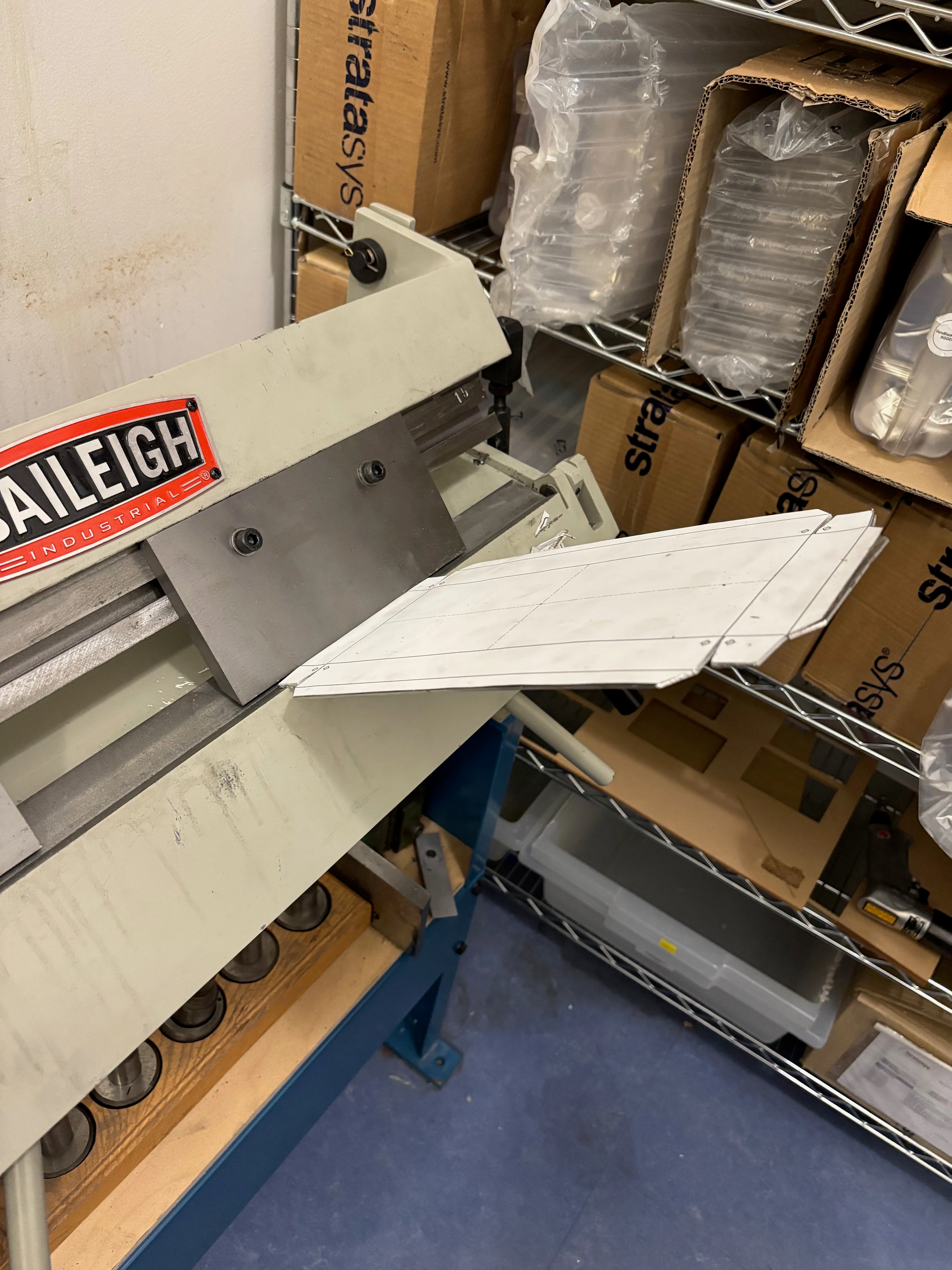 Sheet of aluminum with the paper template stuck on it and about to be placed in a large sheet metal brake